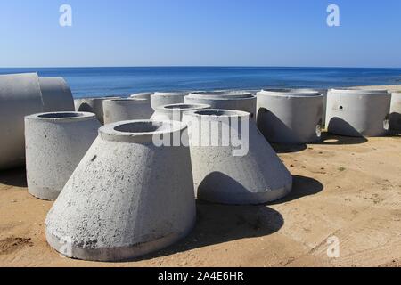 Grand nouveau béton tuyaux circulaires allongé sur une plage de sable pour la construction de système d'assainissement de l'arrière-plan bleu clair de la mer et du ciel Banque D'Images