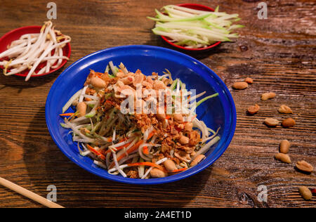 La papaye verte salade de légumes. Délicieuse cuisine Thai servi en plaque bleue sur fond de bois. Banque D'Images