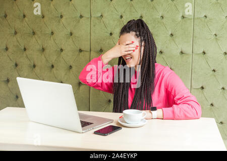 Portrait de peur émotionnelle ou choqué young businesswoman with black dreadlocks hairstyle en blouse rose assis dans un café et couvrant ses yeux et d Banque D'Images