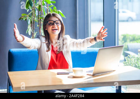 Hug me donner vous. Portrait of happy heureux belle brunette élégante jeune femme à lunettes assis et looking at camera et veulent embrasser l'intérieur. Banque D'Images