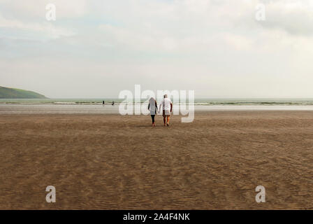 Couple en train de marcher sur une plage de sable en laissant des traces de pas dans le sable. Un père et sa fille profiter de la journée. Jour nuageux. Banque D'Images