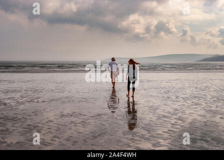 Couple en train de marcher sur une plage de sable en laissant des traces de pas dans le sable. Un père et sa fille profiter de la journée. Jour nuageux. Banque D'Images