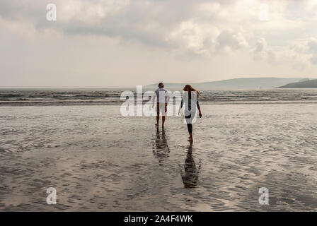 Couple en train de marcher sur une plage de sable en laissant des traces de pas dans le sable. Un père et sa fille profiter de la journée. Jour nuageux. Banque D'Images