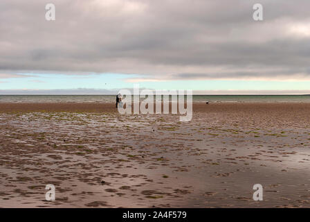 Couple en train de marcher sur une plage de sable en laissant des traces de pas dans le sable. Un père et sa fille profiter de la journée. Jour nuageux. Banque D'Images