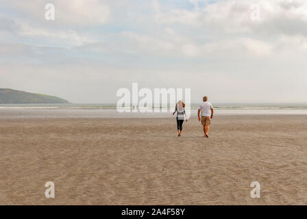 Couple en train de marcher sur une plage de sable en laissant des traces de pas dans le sable. Un père et sa fille profiter de la journée. Jour nuageux. Banque D'Images