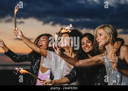 Happy friends avec cierges au coucher du soleil. Quatre laughing friends fête avec feu d'artifice à l'extérieur. Banque D'Images