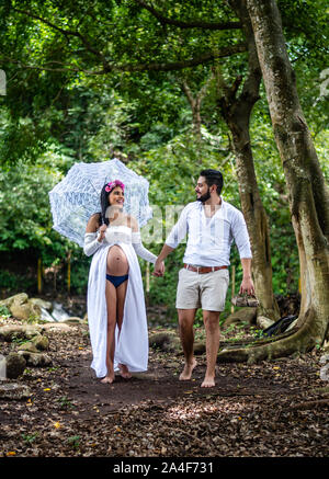 Happy young hispanic couple en train de marcher à l'extérieur. Une femme enceinte avec un parapluie et son mari profitez d'une promenade Banque D'Images