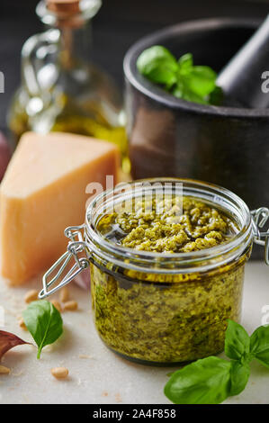 La sauce pesto genovese pesto ou dans un bocal en verre avec les noix de pin, le parmesan, le basilic, l'huile et l'ail sur la planche à découper en marbre blanc. Copier l'espace. Banque D'Images