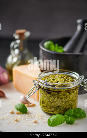 La sauce pesto genovese pesto ou dans un bocal en verre avec les noix de pin, le parmesan, le basilic, l'huile et l'ail sur la planche à découper en marbre blanc. Copier l'espace. Banque D'Images