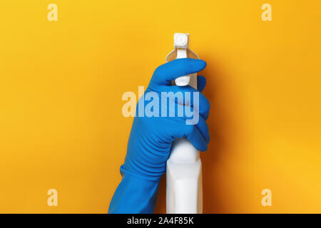 Une main dans un gant de protection latex est titulaire d'un pulvérisateur sur un fond de couleur jaune. Banque D'Images
