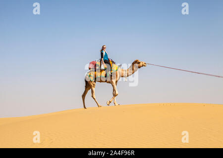 Une femme monté sur un chameau sur une dune de sable dans le désert de Thar, Rajasthan, Inde. Banque D'Images