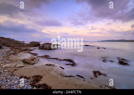 Coucher de soleil avec des nuages filandreux mauve sur Pollan Beach, Inishowen, Irlande. Les roches d'algues et de sable avec vue sur l'horizon sur la péninsule malin Banque D'Images
