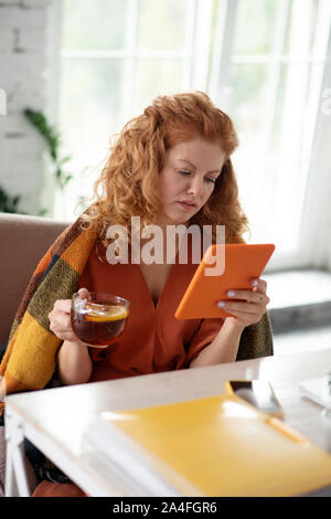 Curly woman holding tablet lors de la lecture de nouvelles en ligne Banque D'Images