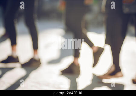 Un flou abstrait arrière-plan des pieds de jeunes personnes marchant sur le trottoir, qui sont éclairés par la lumière vive et projettent de grandes ombres. Banque D'Images