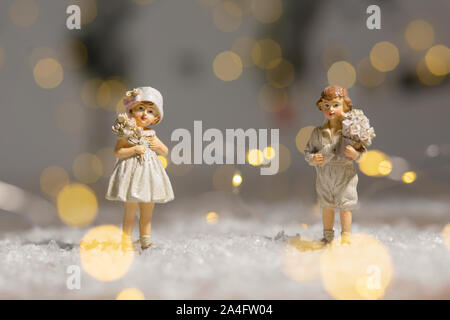 Sur le thème de Noël Décoration figurines. Statuette garçon et fille avec un bouquet de fleurs. Décoration d'arbre de Noël. Décor de fête, chaud bokeh lights Banque D'Images