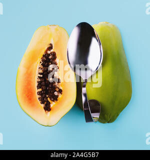 La moitié de la papaye en tranches et cuillère à dessert sur fond bleu, concept d'aliments végétariens. Banque D'Images