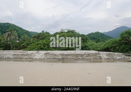 Le Parc National Tayrona beach, un petit cours d'eau s'écoule dans l'avant-plan, dans l'arrière-plan les majestueuses forêts tropicales et les montagnes de la sier Banque D'Images