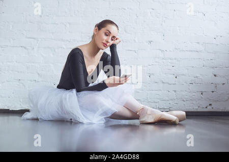 Jeune danseur de ballet assis sur un mur blanc en utilisant le téléphone style de vie actif en studio Banque D'Images