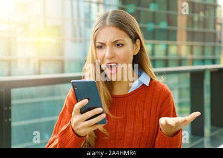 Déçu femme en colère mauvaise réception du contenu en ligne sur téléphone mobile marche dans la rue. Banque D'Images