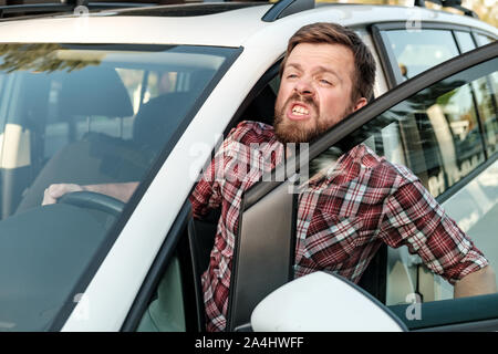 Un pilote d'ennuyé a ouvert la porte de sa voiture et crie à quelqu'un. Close-up. Banque D'Images