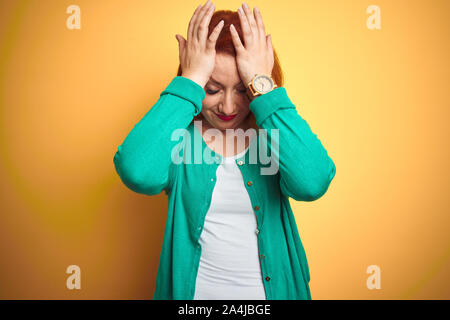 Belle jeune femme rousse portant chandail vert d'hiver isolé sur fond jaune qui souffrent de maux de tête désespéré et a souligné parce que la douleur Banque D'Images