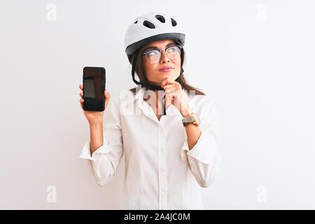 Young Woman holding smartphone casque de vélo sur fond blanc isolé visage sérieux de penser à question, idée très confus Banque D'Images