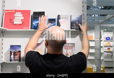 15 octobre 2019, Hessen, Frankfurt/Main : Un homme au Salon du livre de Francfort sortes livres dans une étagère. La Norvège est le pays invité cette année à la Foire du livre. Photo : Silas Stein/dpa Banque D'Images