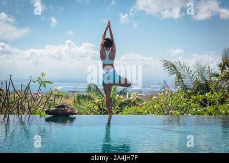 Young woman practicing yoga asanas posent sur le bord de piscine à débordement avec vue imprenable à la villa à Bali Banque D'Images