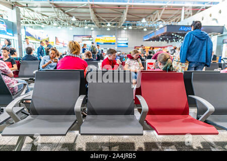 L'Aéroport International d'Almaty à trois sièges vides près de la porte de départ tout en arrière-plan une femme utilise son smartphone Banque D'Images