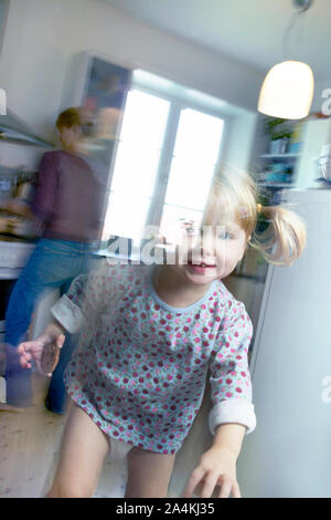 Impatients, deux ans active girl jumping, pendant que la mère fait l'alimentation. Banque D'Images