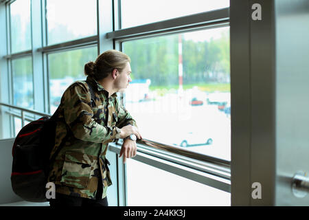 Jeune homme debout avec tourisme sac à dos à la salle d'attente de l'aéroport, le port de chemise de camouflage. Banque D'Images