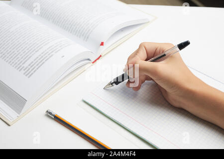 La main de l'enfant tenant un stylo écrit sur une feuille de papier blanc. lycéenne part avec stylo et ordinateur portable Banque D'Images