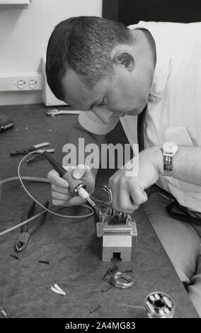 Années 1960, historique, un étudiant adulte travaillant dans un atelier, utilisant un fer à souder sur une boîte à fusibles électrique, USA. Banque D'Images