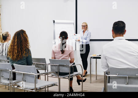Smiling manager passe plus de graphiques et tableaux au cours d'une présentation au personnel dans une salle de réunion dans un bureau