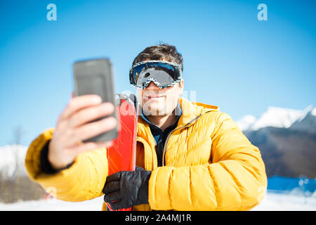 Photo de smiling man in ski mask à prendre des photos de lui-même dans l'après-midi contre le ciel bleu et arbres Banque D'Images