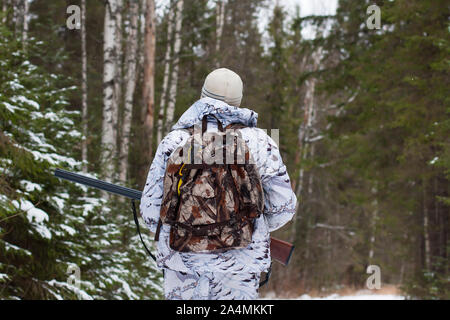 Hunter with gun marche dans la forêt d'hiver Banque D'Images