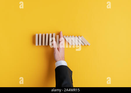 Vue de dessus de crise d'entreprise manager l'arrêt de la chute des dominos avec sa main dans une image conceptuelle. Sur fond jaune avec copie espace. Banque D'Images