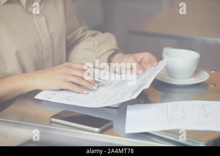 Close-up de jeune femme assise à la table avec une tasse de café et le téléphone mobile et la lecture de documents d'affaires Banque D'Images