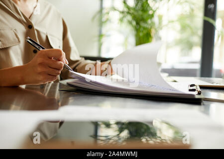 Close-up de manager à la table tenir pen et prendre des notes dans des documents papier qu'elle fait travailler au bureau Banque D'Images