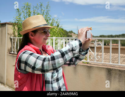 Touristiques attrayants fille prend une photo sur son téléphone portable tout en se tenant dans la rue. Banque D'Images