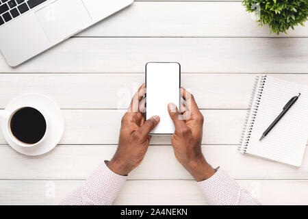 Homme noir en utilisant smartphone moderne avec écran vide sur le lieu de travail Banque D'Images