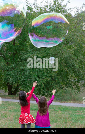 Deux jeunes filles atteignant et tente de prendre des bulles géantes. Banque D'Images