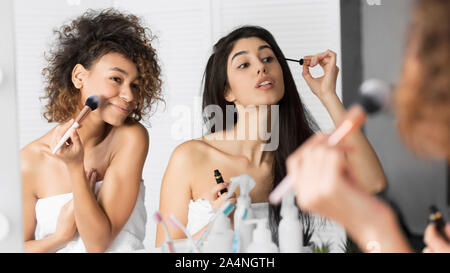 Deux filles millénaire appliquant le maquillage dans la salle de bains, Panorama Banque D'Images
