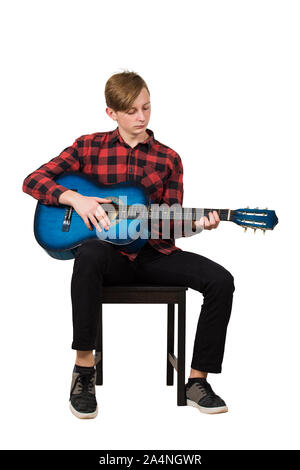 Portrait de l'adolescent garçon talentueux à jouer sur la guitare acoustique assis sur une chaise isolée sur fond blanc. Beaucoup de leçons de musique fo Banque D'Images