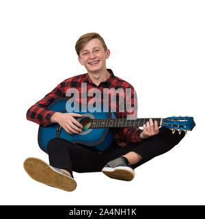Portrait de l'adolescent garçon talentueux à jouer sur la guitare acoustique assis sur le plancher isolé sur fond blanc. Beaucoup de leçons de musique f Banque D'Images