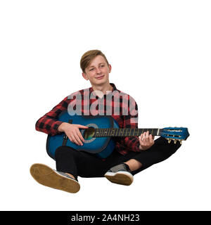 Portrait de l'adolescent garçon talentueux à jouer sur la guitare acoustique assis sur le plancher isolé sur fond blanc. Les leçons de la grande musique Banque D'Images