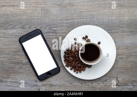 Tasse de café avec des haricots sur une table en bois avec un smartphone avec écran blanc pour le message Banque D'Images