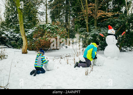 Père avec peu de fils de croisière snowman dans city park Banque D'Images