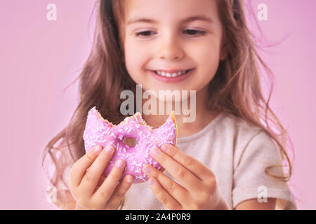 Happy little girl eating donut rose sur fond rose Banque D'Images