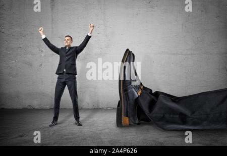 Petit homme debout avec les bras près de jambe géant d'un autre homme Banque D'Images